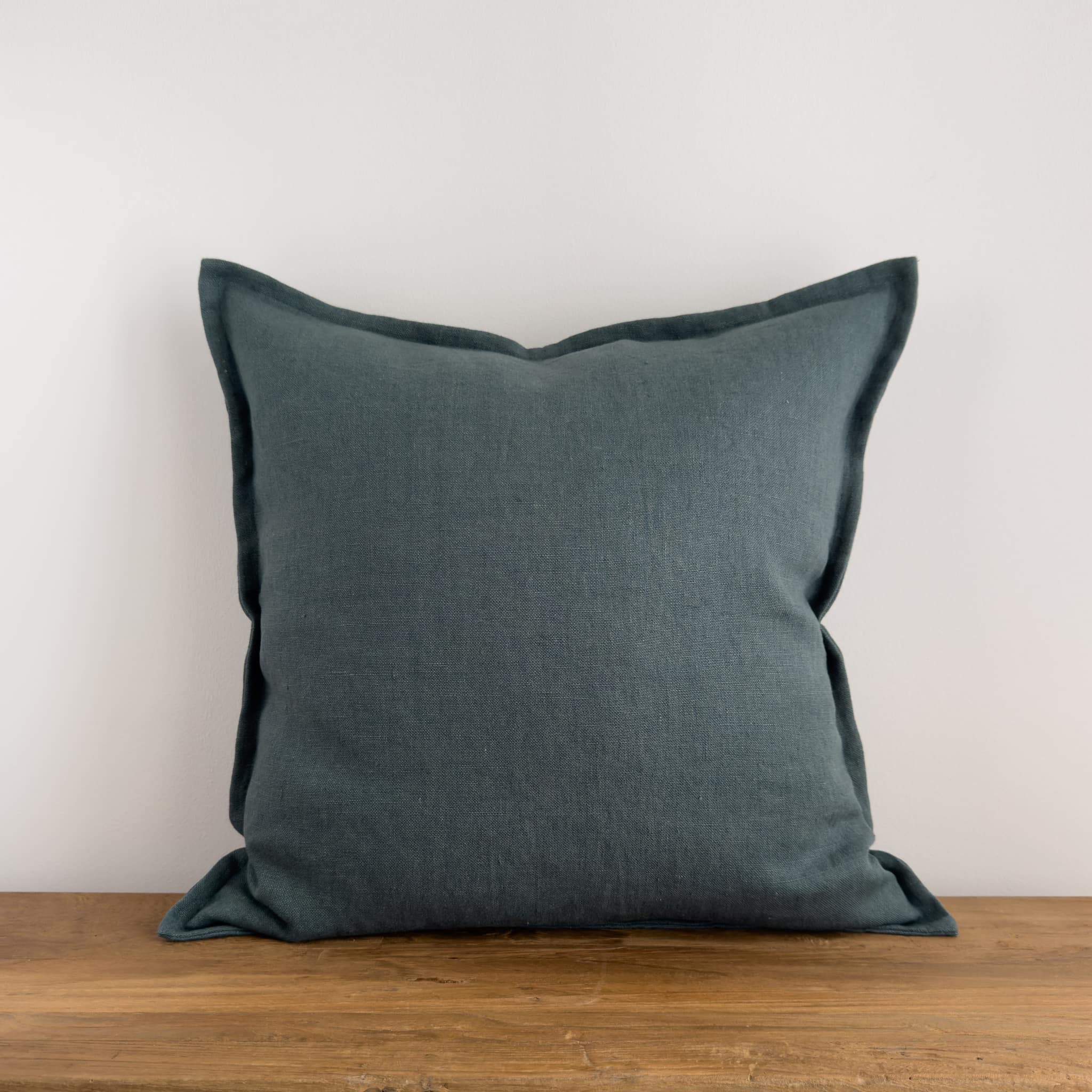 Teal blue stonewashed linen cushion on a rustic wood bench