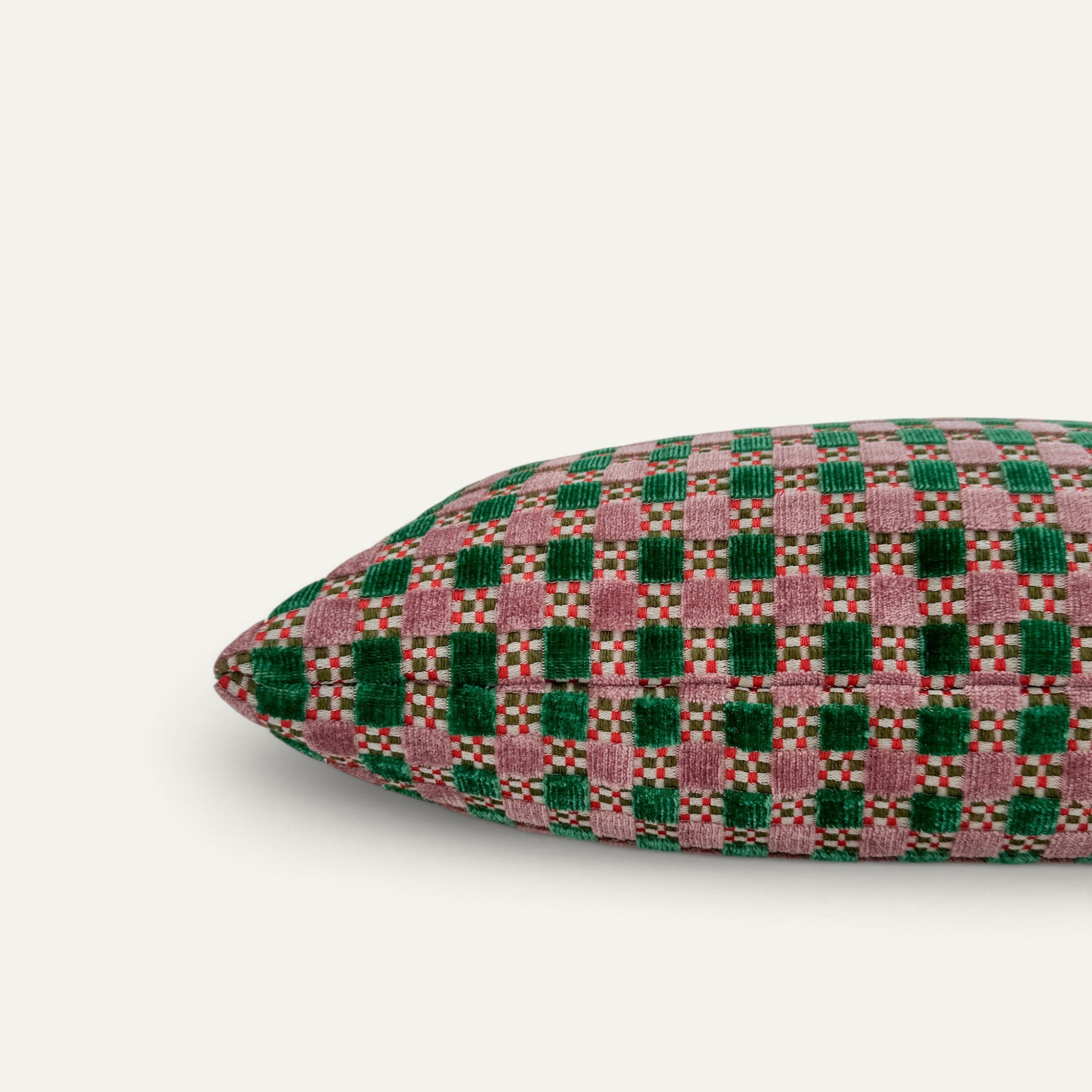 A close-up of a throw pillow featuring a woven checkered pattern in green and dusty pink velvet, shown against a plain off-white background.
