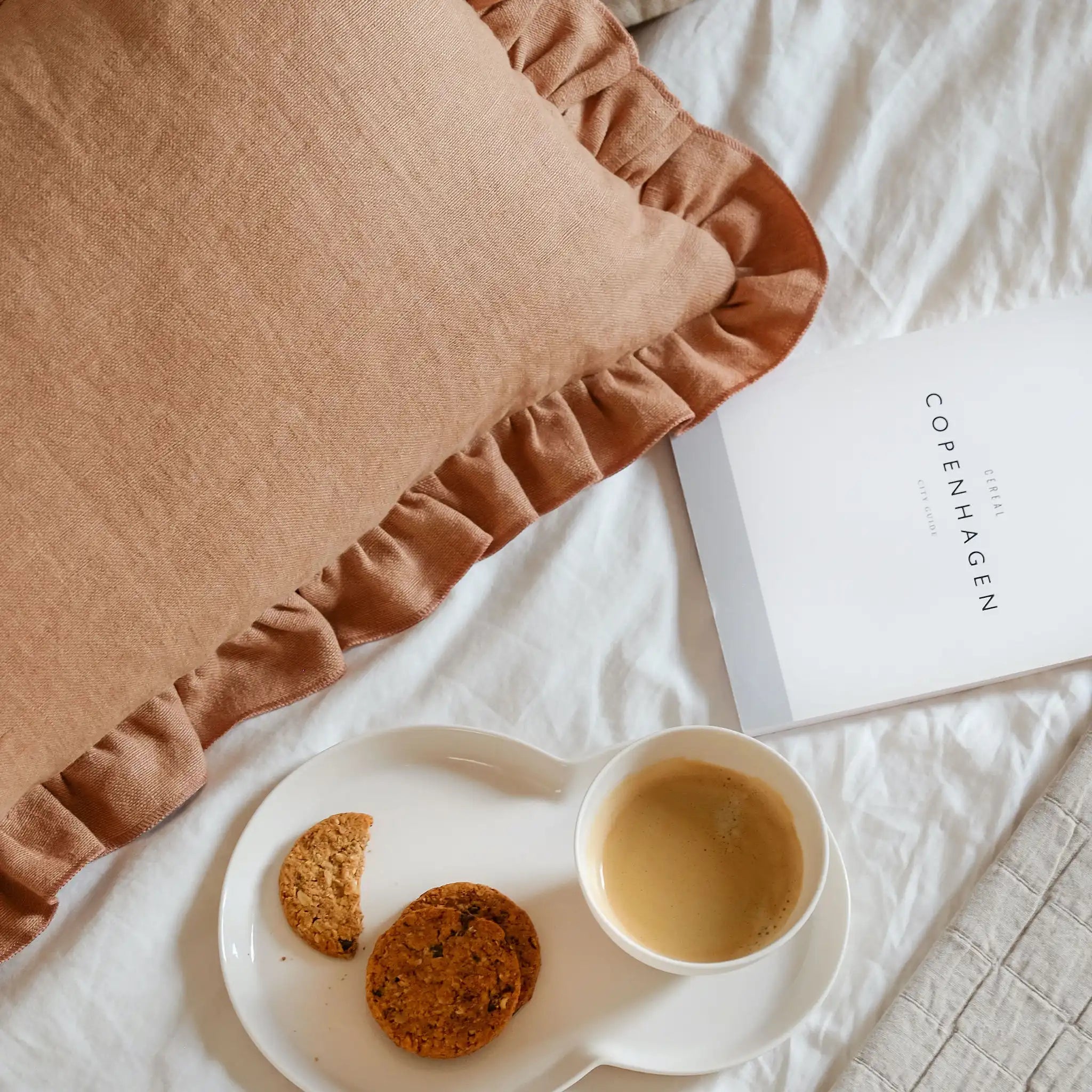 Clay brown linen cushion with ruffled edge on cosy bed