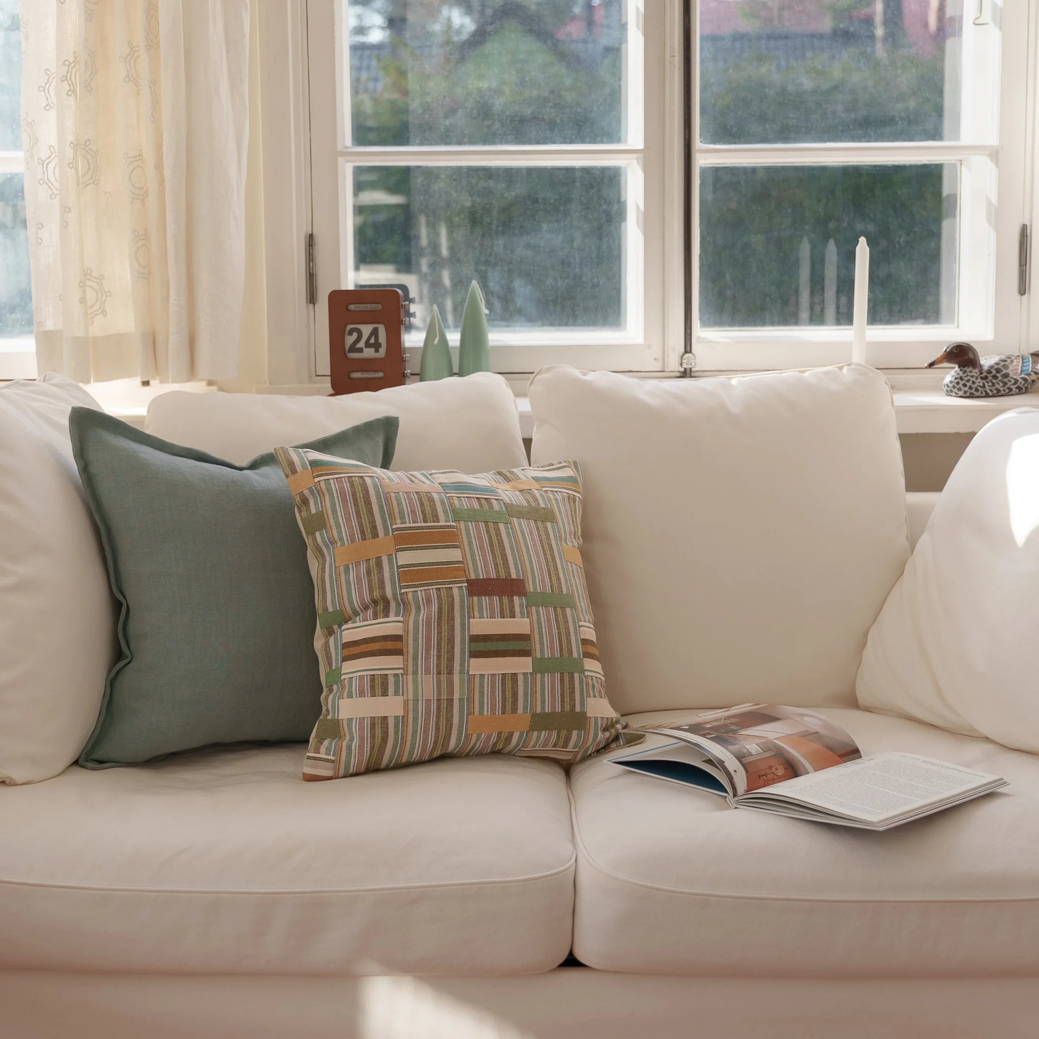 Patchwork Ewe Kente Clothe inspired cushion and light blue linen cushion on a warm and cosy white sofa.