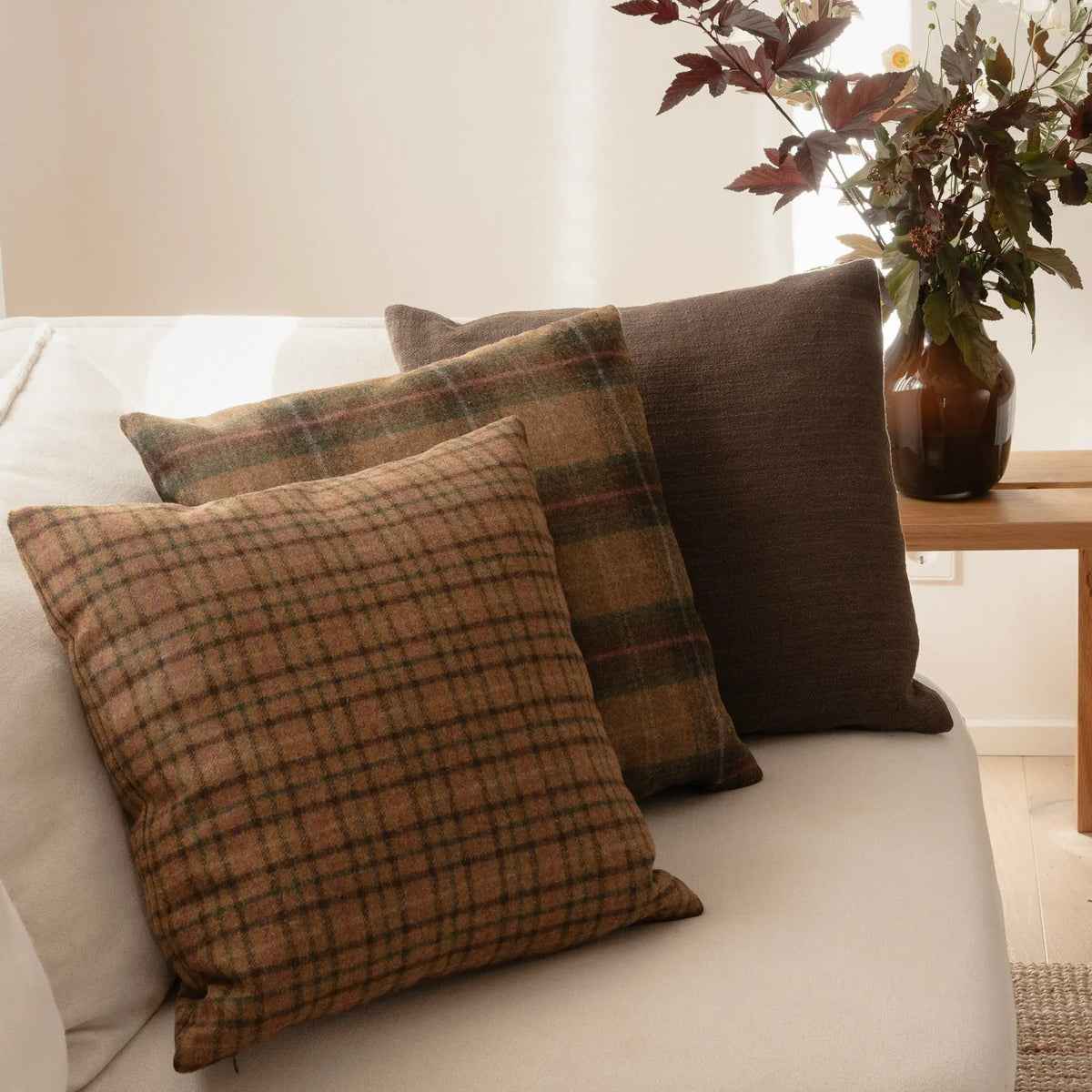Hazel wool check cushion cover on a cream sofa, layered with a green wool check and a brown cushion beside autumn branches