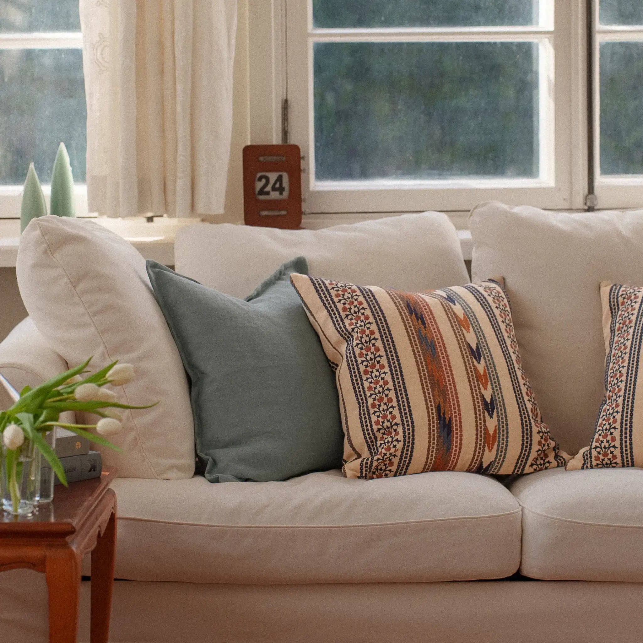 Light blue plain cushion and embroidered floral cushion styled on a white sofa