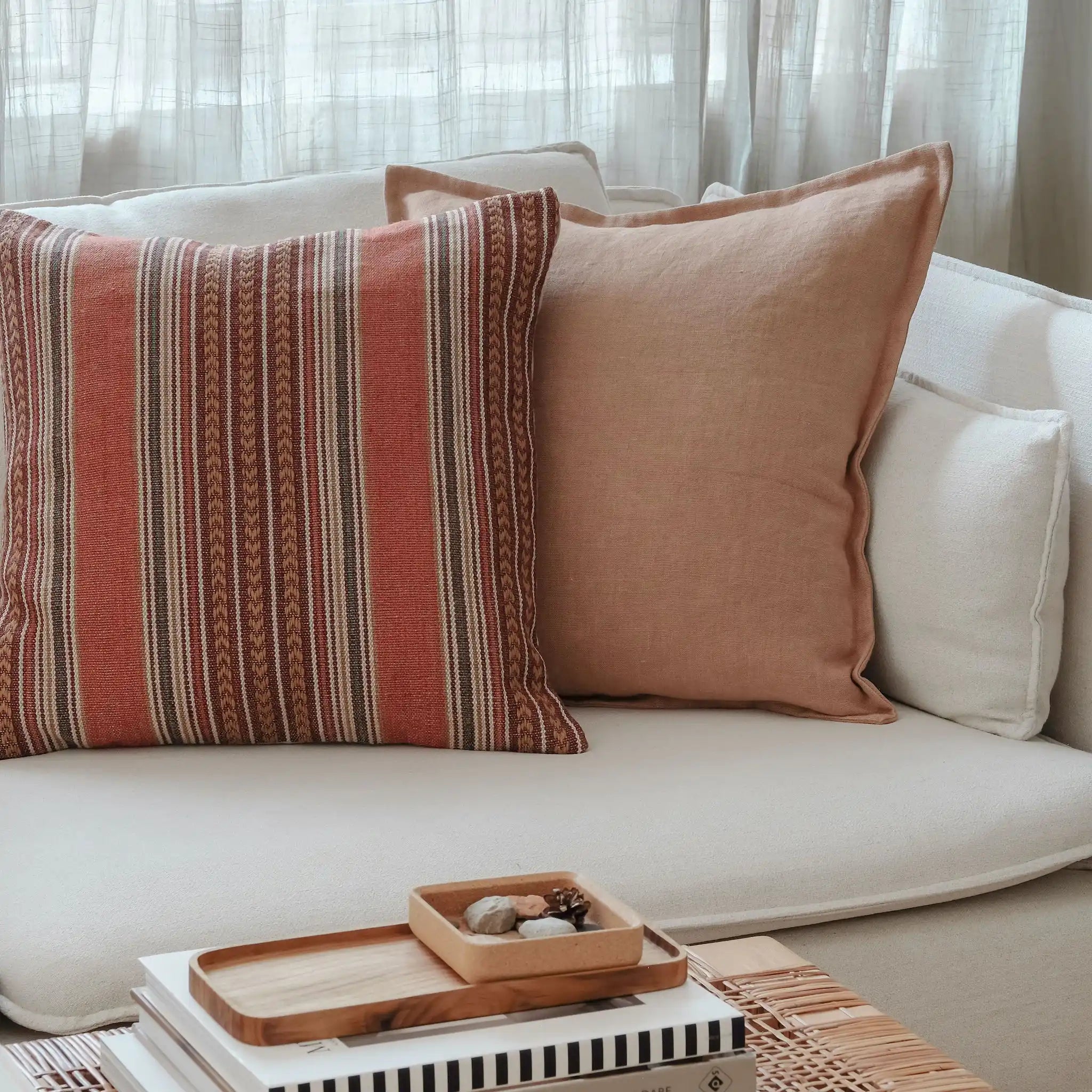 Clay brown linen cushion and rust-toned patterned cushion styled on a white sofa