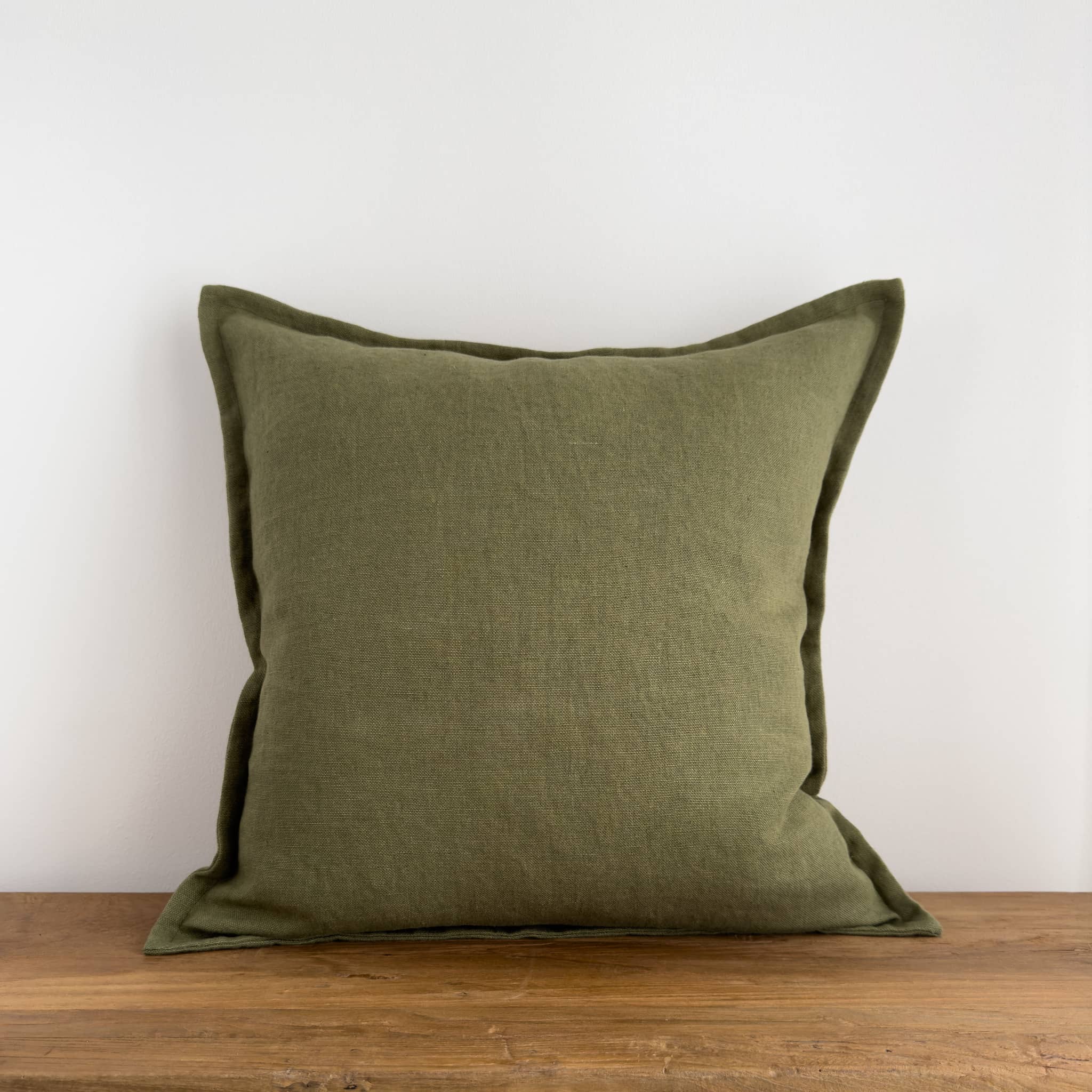 Olive green linen cushion cover on a rustic wood bench