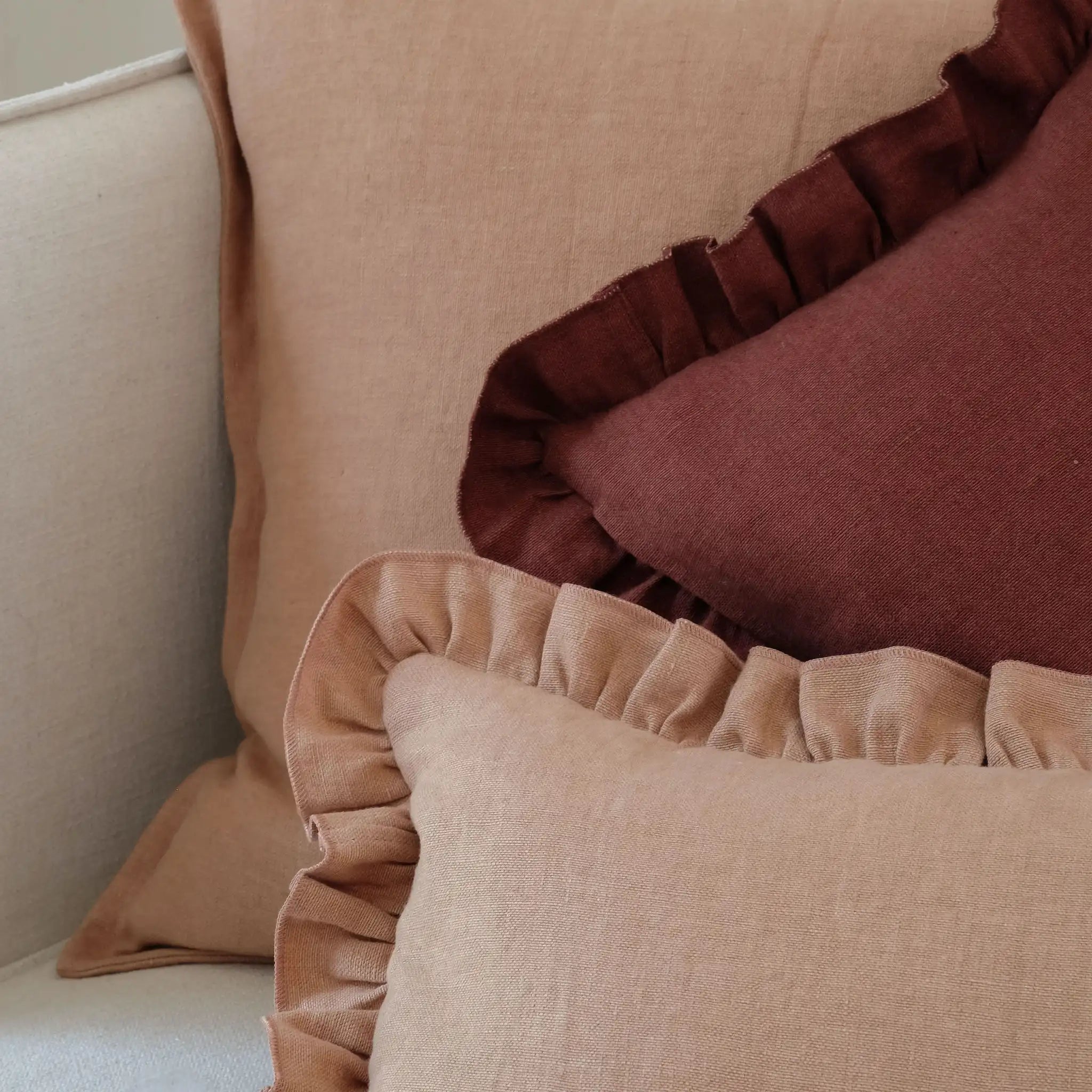 Clay brown and burgundy linen cushions with ruffled edges, layered together on a sofa