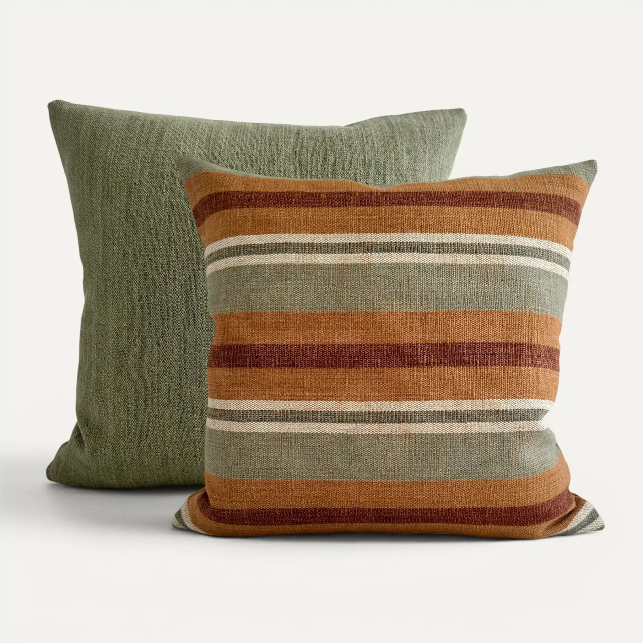 Two square throw pillows on a light gray background. The front pillow has horizontal stripes in rust orange, olive green, cream, and dark red-brown, while the back pillow is a solid muted sage green.