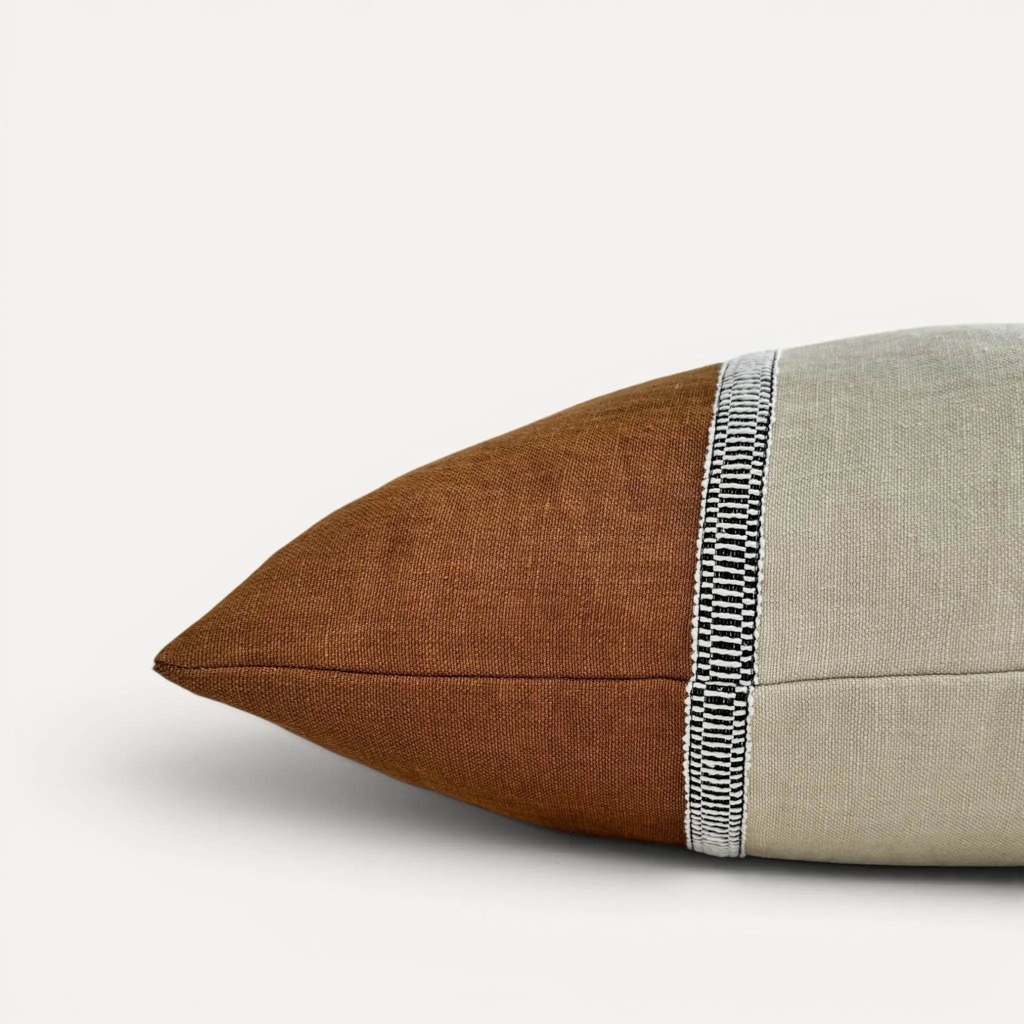 Side view of cream and brown linen cushion cover with black and white striped decorative ribbon